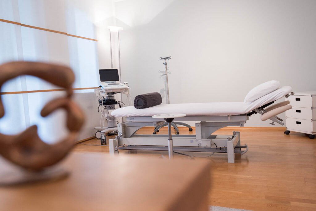 Helles Behandlungszimmer mit Liege und Ultraschallgerät